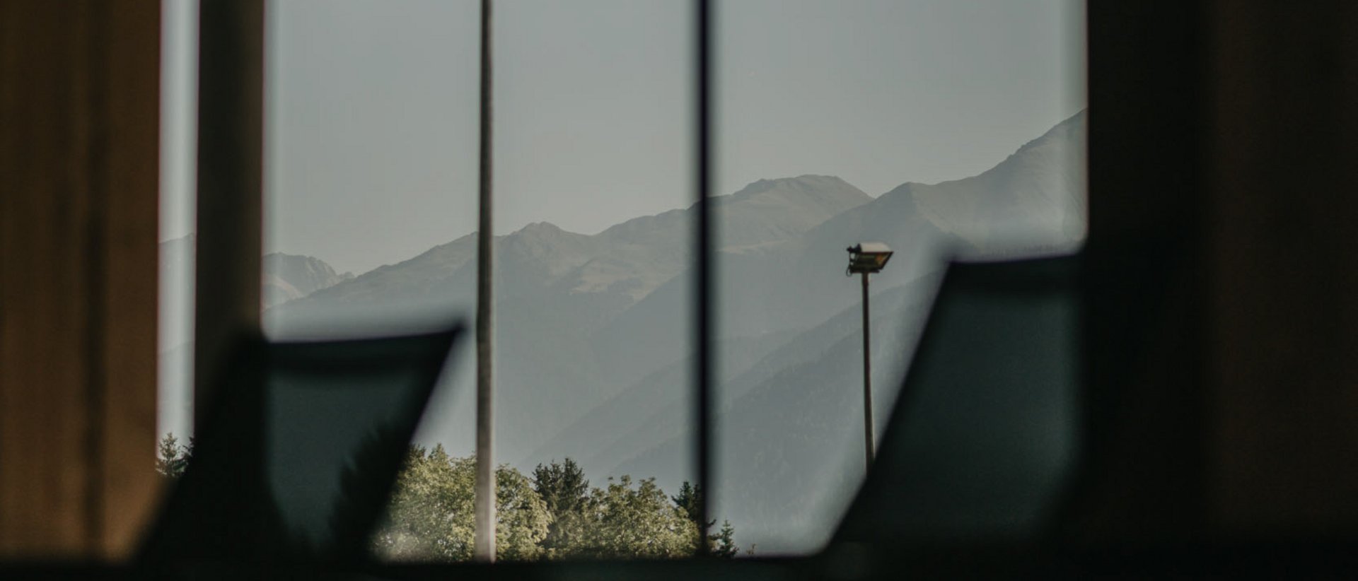 Honigmassage Bergblick durch großes Fenster in dunklem Innenraum mit Stühlen