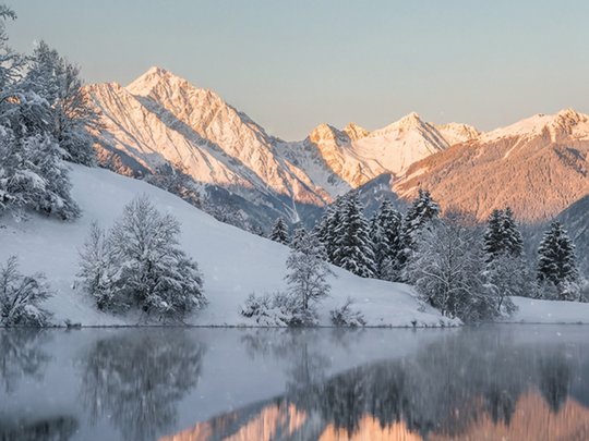 Una giornata di relax Montagne e alberi innevati riflessi in lago calmo al tramonto.