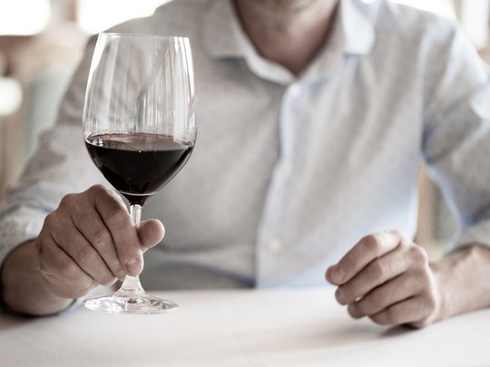 Regionale, alpine Küche im Hotel am Kronplatz in Südtirol Mann hält ein Glas Rotwein in der Hand, Fokus auf dem Glas