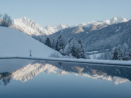 Big changes at your Lago di Braies/Pragser Wildsee accommodation Snow-covered mountains reflected in a calm lake under a clear blue sky