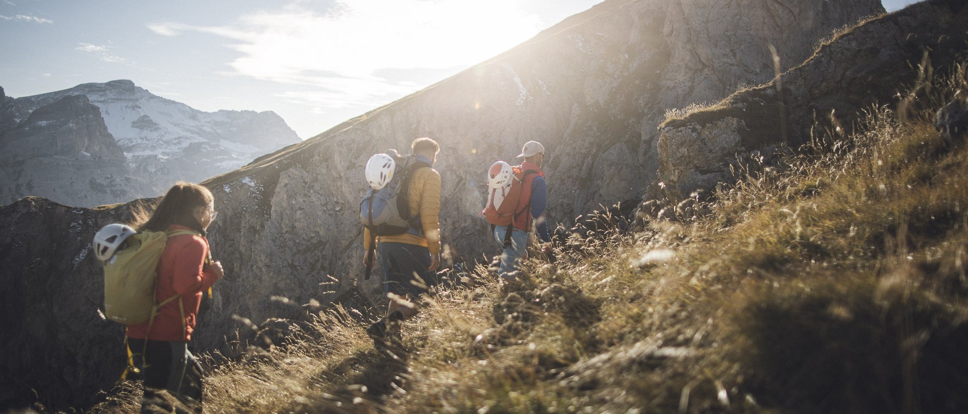 Urlaub im Herbst – die beste Reisezeit für Südtirol Drei Wanderer mit Helmen auf einem sonnigen Bergpfad