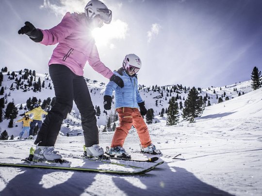 Unforgettable skiing holiday on Plan de Corones/Kronplatz Adult teaching child to ski on snowy mountain in bright sunshine