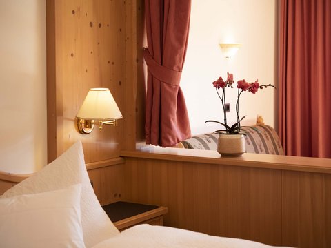 Vorbei am Pragser Wildsee zum Hotel: Ihr Weg in den Urlaub Gemütliches Hotelzimmer mit Holzverkleidung und Orchidee auf der Trennwand