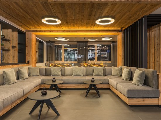 A warm welcome to our hotel in Olang, at Plan de Corones/Kronplatz Modern lounge with gray sectional sofa and fireplace with wooden interior