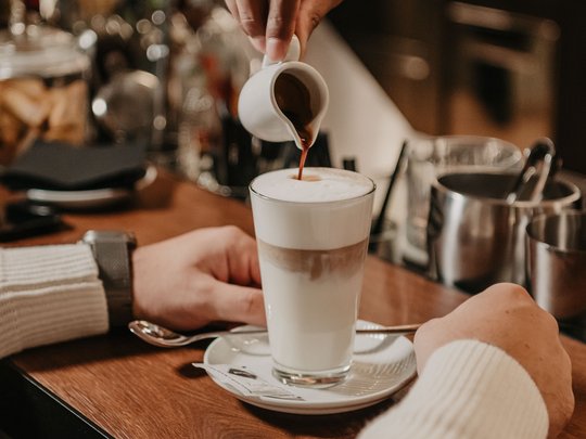 Concedetevi una pausa Mano che versa espresso in un bicchiere di latte macchiato in un bar