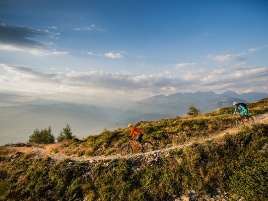 Novità dal nostro hotel al Plan de Corones Due ciclisti in mountain bike su un sentiero di montagna con panorama alpino