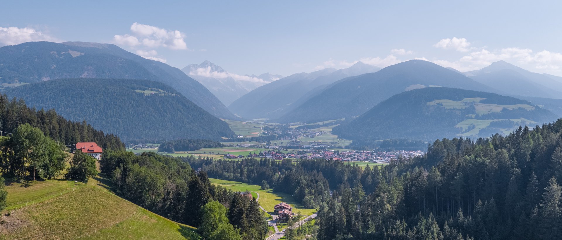Wandersaison im Pustertal Bergtal mit Dorf, Wald und Straße unter klarem Himmel