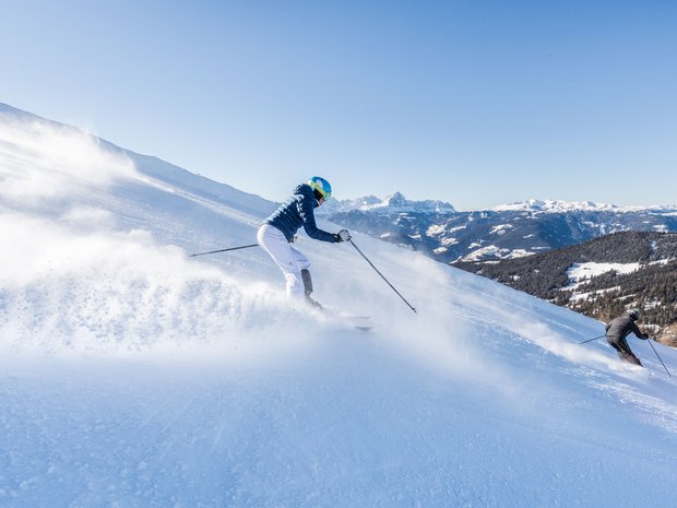 Unforgettable skiing holiday on Plan de Corones/Kronplatz Two skiers skiing down a snowy mountain slope on a clear day