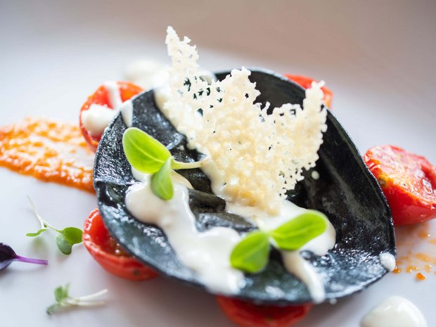 Sustainable 4-star hotel in the Dolomites Gourmet dish with black pasta, tomatoes, cream cheese, and herbs