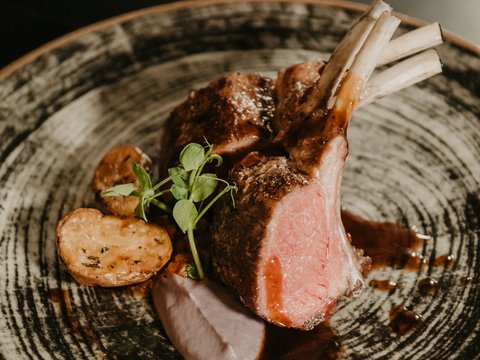 Regionale, alpine Küche im Hotel am Kronplatz in Südtirol Gegrillte Lammkoteletts mit Kartoffeln und Sauce auf einem dekorativen Teller