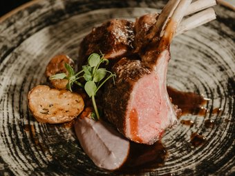 Inklusivleistungen Ihres Dolomiten-Wellnesshotels Gegrillte Lammkoteletts mit Kartoffeln und Sauce auf einem dekorativen Teller
