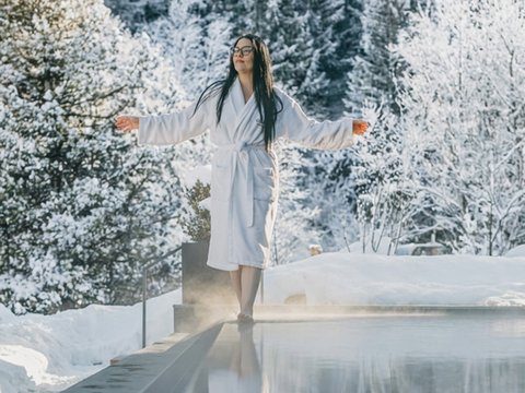 Fitness am Pragser Wildsee: Übernachtung im Hotel Christoph Frau im Bademantel am Rand eines dampfenden Pools mit schneebedecktem Wald