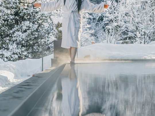 Una giornata di relax Donna in accappatoio vicino a piscina calda con bosco innevato sullo sfondo