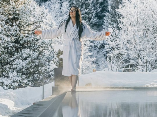 Una giornata di relax Donna in accappatoio vicino a piscina calda con bosco innevato sullo sfondo