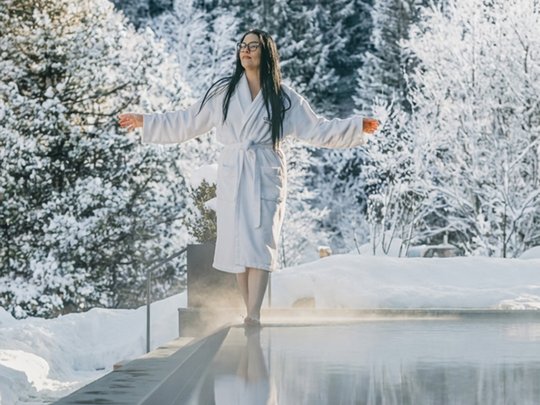 Day Spa Frau im Bademantel am Rand eines dampfenden Pools mit schneebedecktem Wald