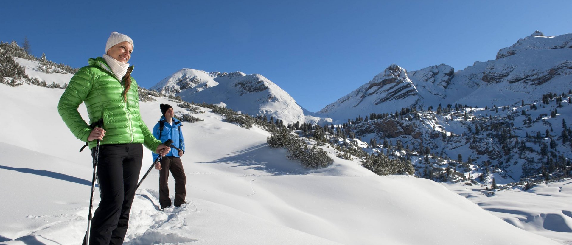 Vacanza invernale da sogno Due escursionisti con abbigliamento invernale camminano tra montagne innevate con cielo sereno