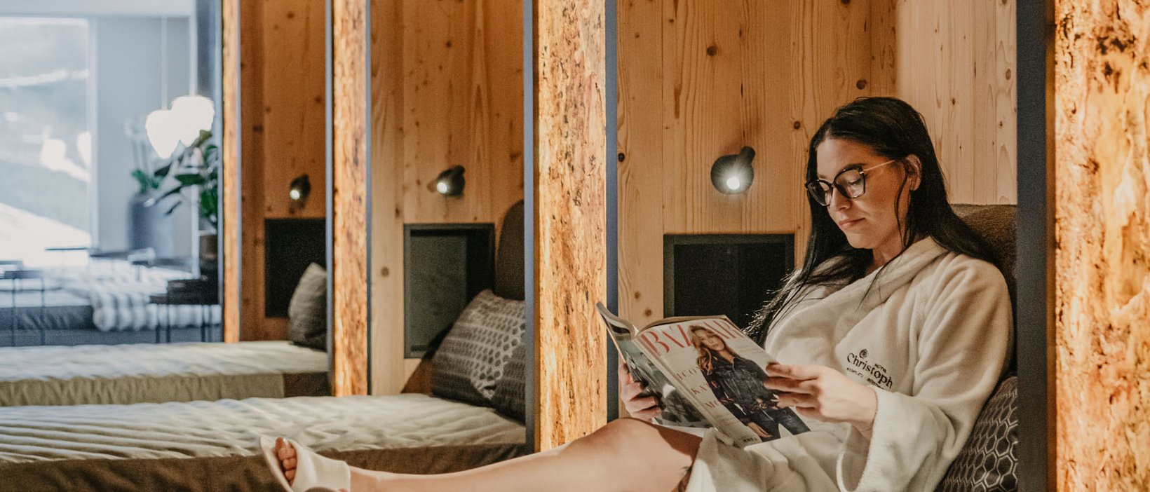 Day Spa Frau in Bademantel liest Magazin auf Liege in modernem Ruheraum