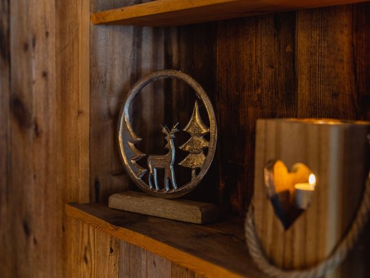 Hotel Christoph:immergetevi in in’atmosfera di benessere! Mensola in legno con decorazione in metallo di cervo e alberi accanto a portacandele di legno a forma di cuore