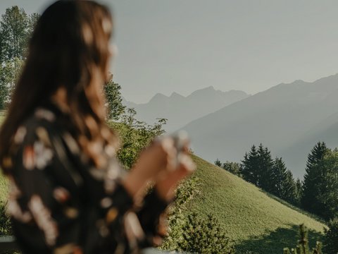 Willkommen in Olang: Hotel Christoph Frau mit Tasse auf Balkon blickt auf grüne Hügel und Berge im Hintergrund