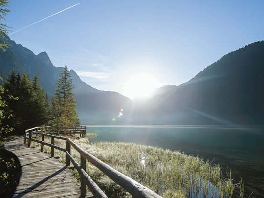 Novità dal nostro hotel al Plan de Corones Passerella in legno sul lago con montagne e alba sullo sfondo