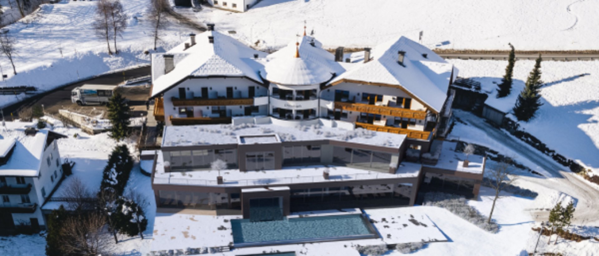 Weihnachtsgrüße von Familie Lanz Verschneites Hotel mit Außenpool in einer winterlichen Berglandschaft