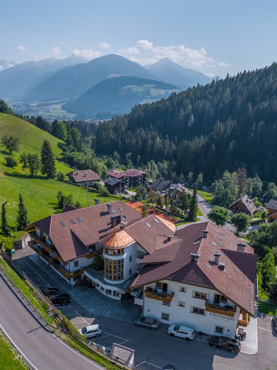 Willkommen in Olang: Hotel Christoph Hotel Christoph mit Bergkulisse und Wald in sonniger Landschaft