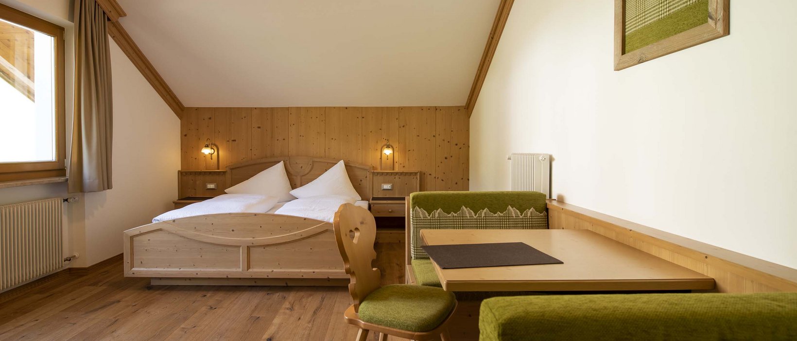 Info e prezzi del nostro hotel benessere nelle Dolomiti Camera accogliente con pareti in legno e zona pranzo verde