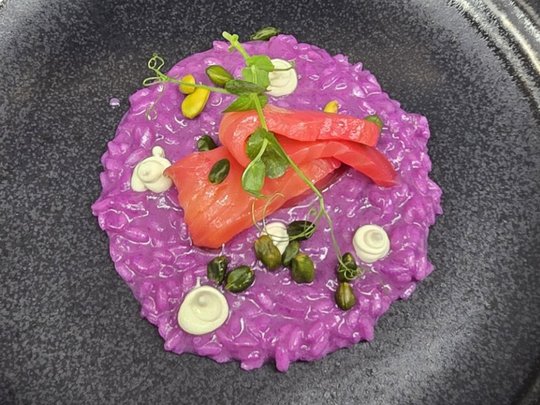 Regionale, alpine Küche im Hotel am Kronplatz in Südtirol Lila Risotto mit Lachs, Kapern und grünen Kräutern auf schwarzem Teller