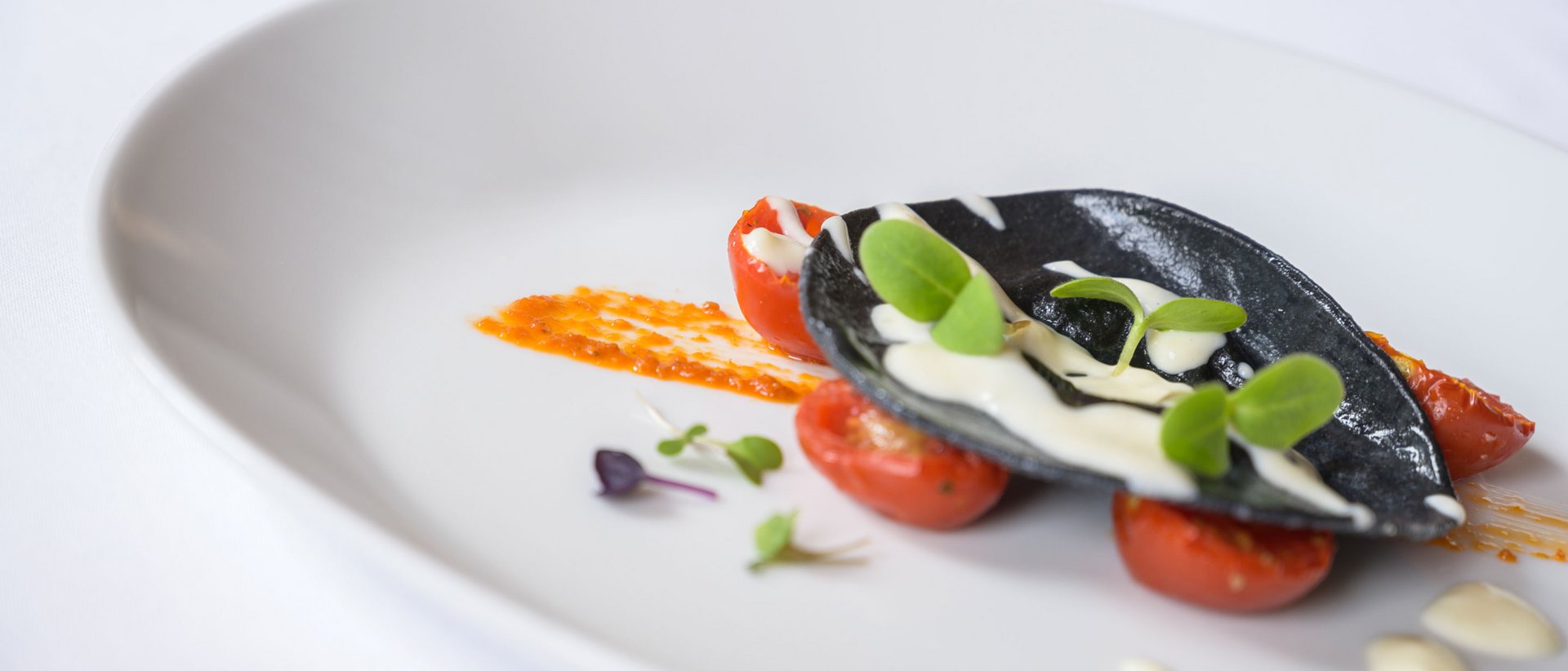 La nostra pensione ¾ Ravioli neri con pomodori, foglie verdi e salsa bianca su piatto bianco