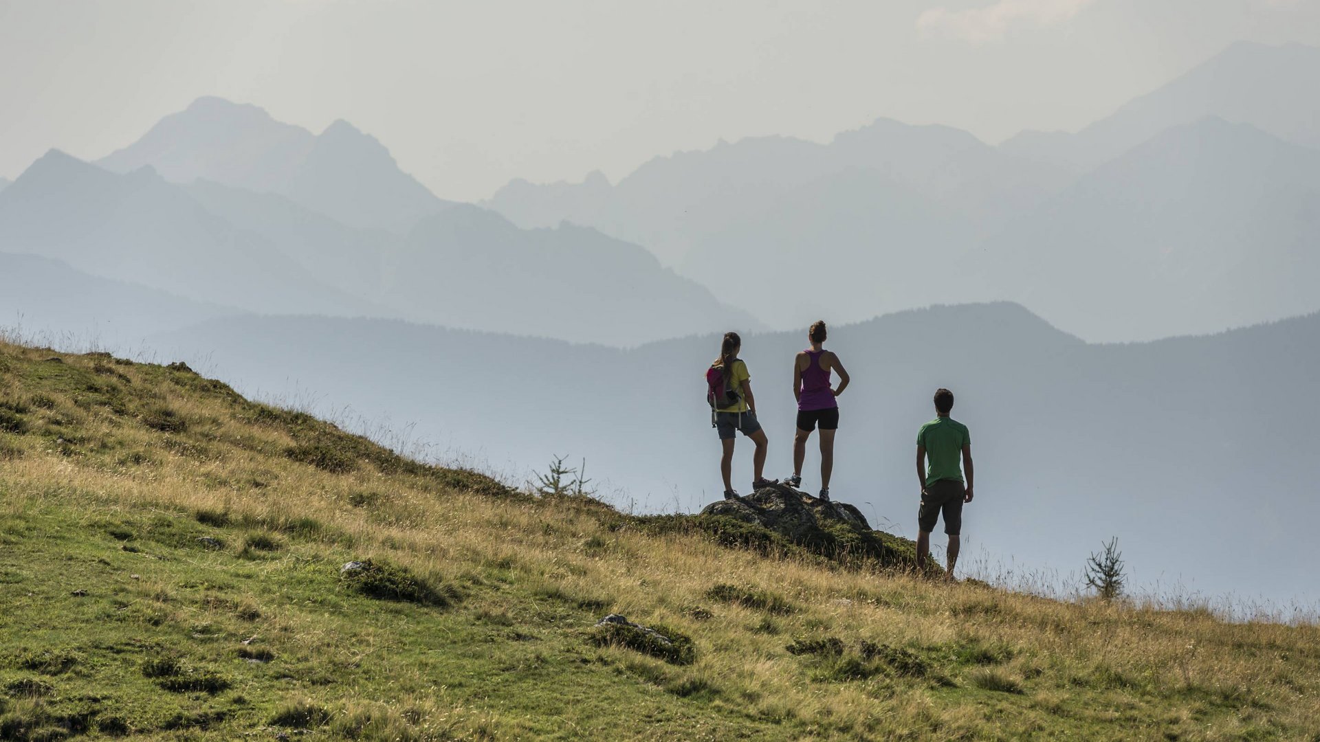Escursioni, arrampicate e wellness a Valdaora Tre escursionisti in piedi su un prato guardano una paesaggio montano nebbioso