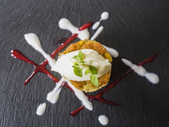 Regionale, alpine Küche im Hotel am Kronplatz in Südtirol Ein kleiner gebratener Snack mit weißer Creme und Kräutern auf schwarzem Teller