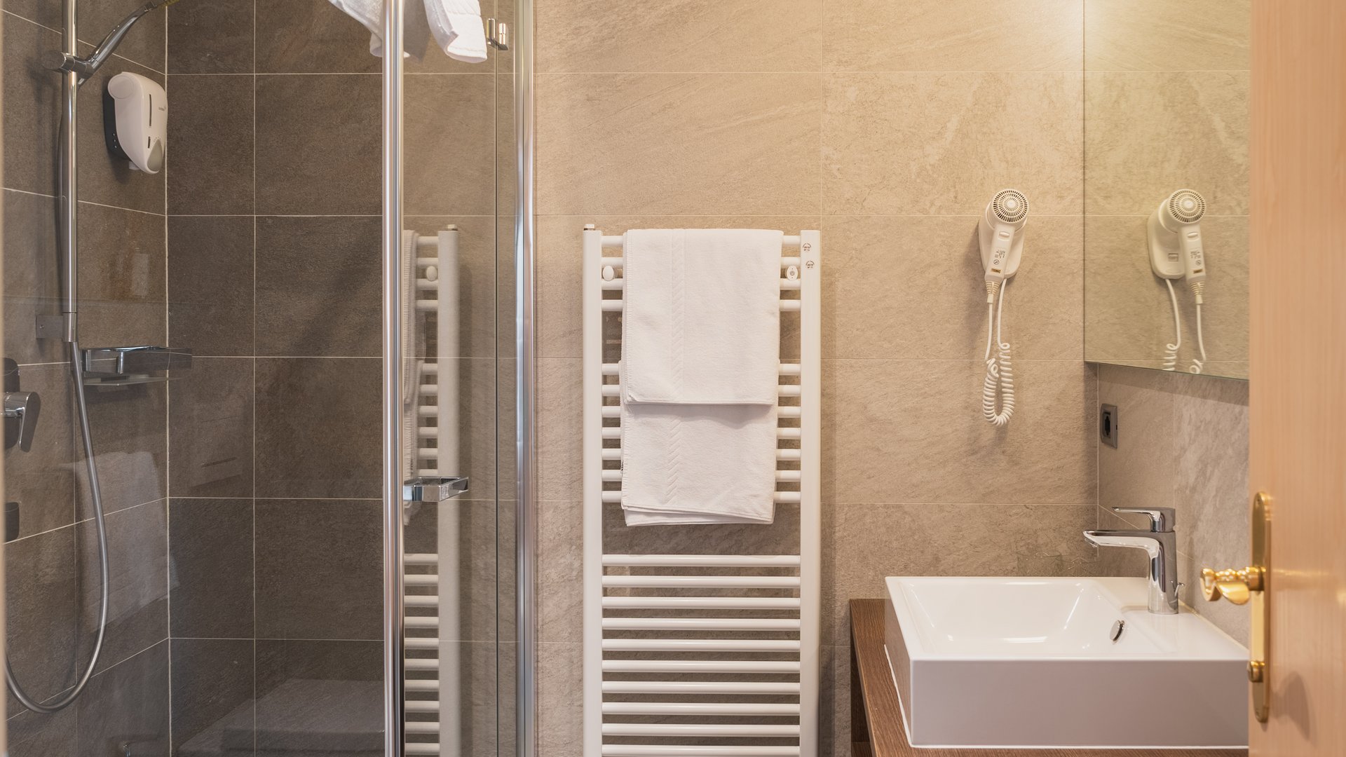 Servizi inclusi nel nostro wellness hotel al Plan de Corones Bagno moderno con doccia in vetro, lavabo bianco e asciugamani bianchi