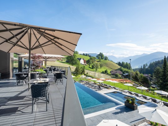 Le novità del nostro hotel a 4 stelle tra le Dolomiti Terrazza con tavoli e ombrelloni accanto alla piscina con vista sulle montagne