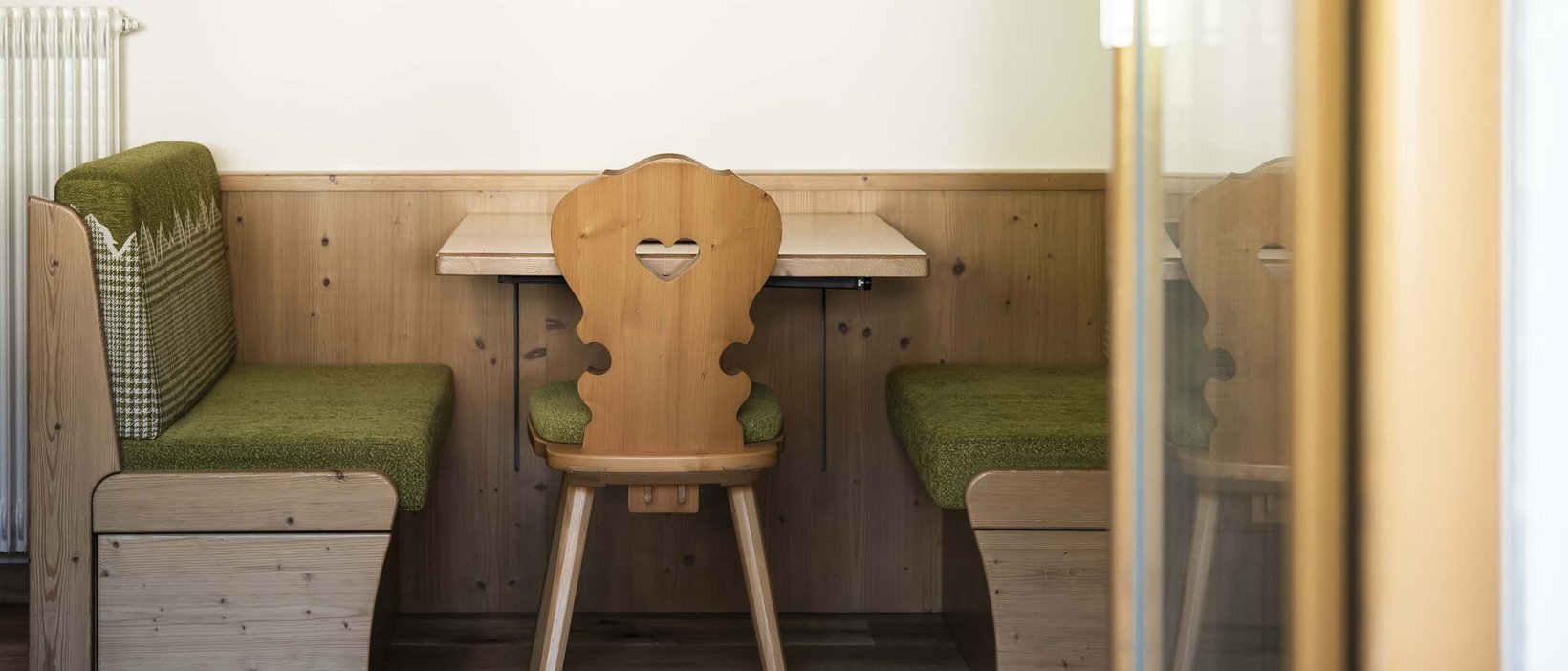 Hotel Christoph:immergetevi in in’atmosfera di benessere! Panca in legno con cuscino verde e sedia in legno con cuore in un ristorante