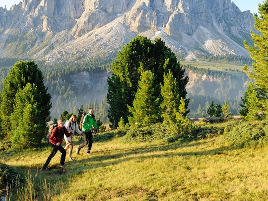 Novità dal nostro hotel al Plan de Corones Tre escursionisti su prato verde con montagne rocciose e cielo blu