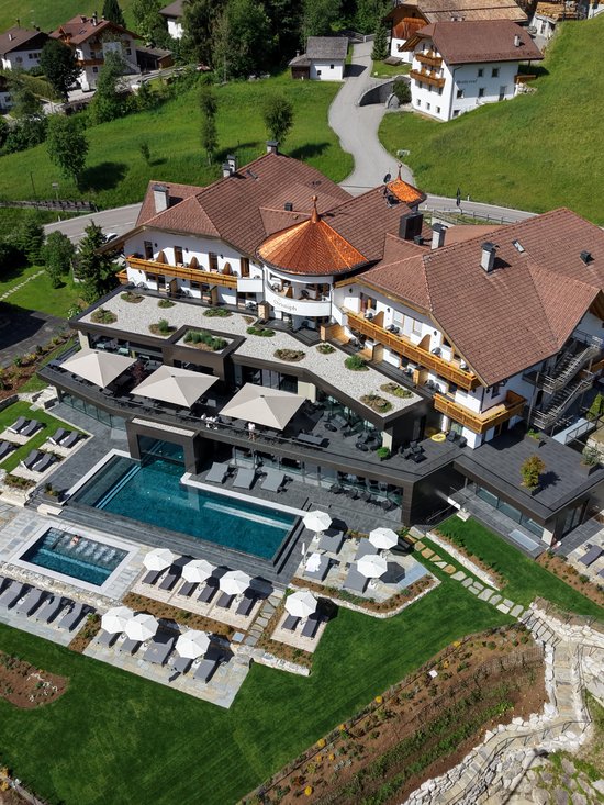 4-Sterne-Hotel am Kronplatz: Ihr perfektes Urlaubszuhause Luftaufnahme eines Hotels mit Pool, Sonnenschirmen und Liegestühlen auf grünem Rasen