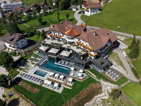 Der Kronplatz aus nächster Nähe: Ihr Aktivhotel in Südtirol Luftaufnahme eines Hotels mit Pool, Sonnenschirmen und Liegestühlen auf grünem Rasen