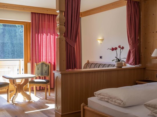 Hotel Christoph:immergetevi in in’atmosfera di benessere! Camera d'hotel accogliente con mobili in legno, angolo soggiorno e balcone con vista foresta