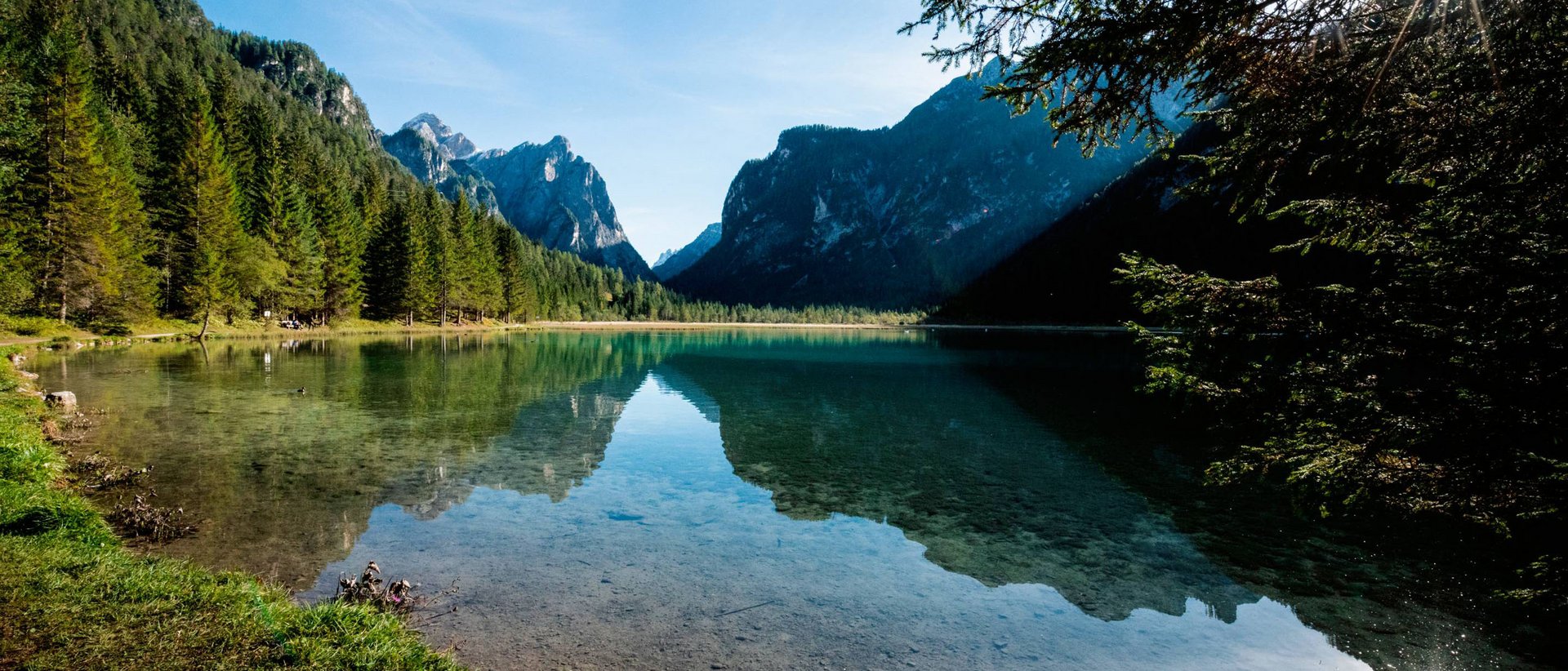 Ausflugstipps: Toblacher See Klarer Bergsee mit Nadelbäumen und Sonnenlicht im Hintergrund
