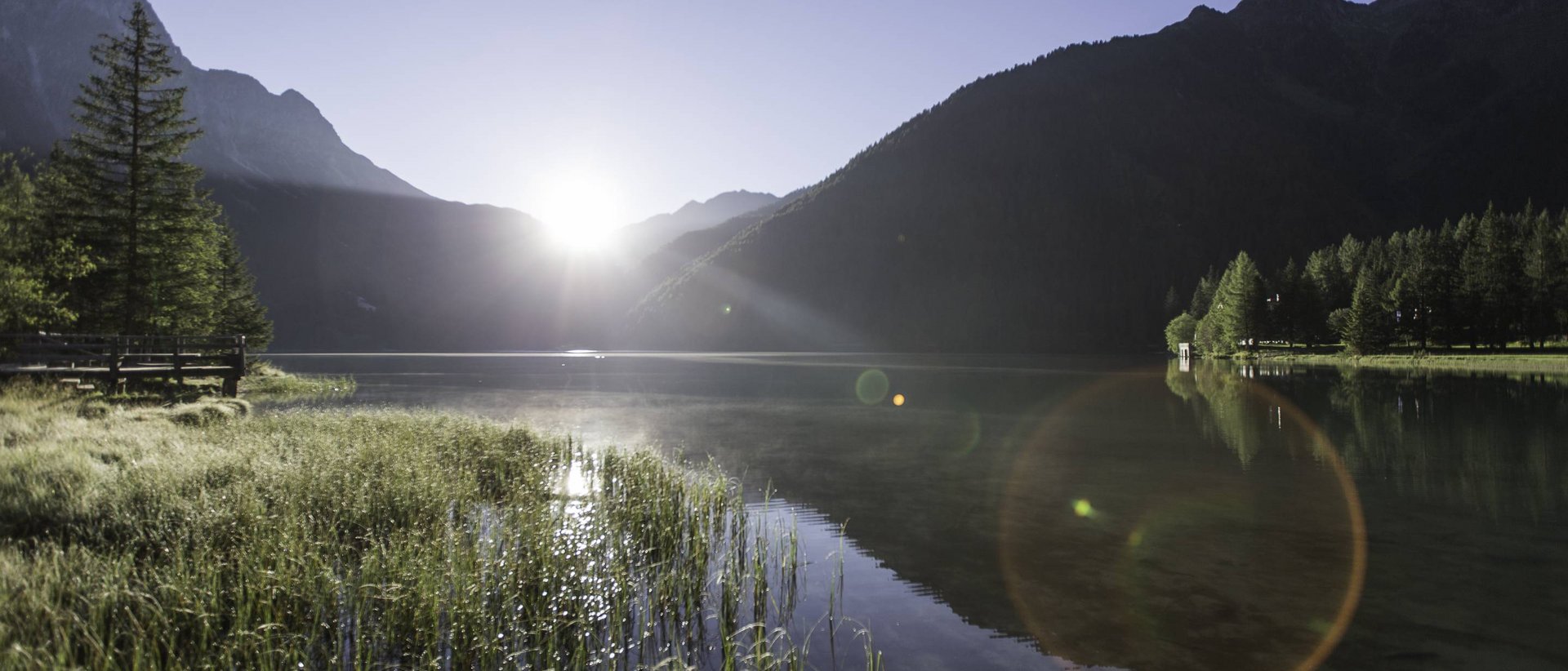 Bewusstes und umweltfreundliches Reisen Sonnenaufgang über einem Bergsee mit Gras und Bäumen am Ufer